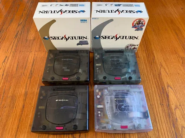 Sega Saturn in Translucent Black, White, Grey and a lighter Grey variant with their respective boxes behind them.